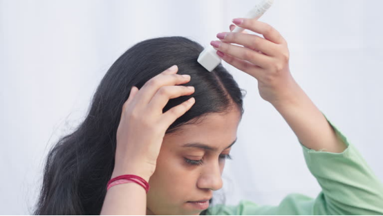 Woman applying a hair wax stick to her hair (for frizz control in humid weather).