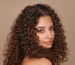 A woman with smooth, defined curls, showcasing the frizz-free, polished results a hair wax stick delivers for curly hair.