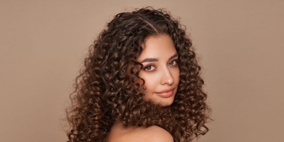 A woman with smooth, defined curls, showcasing the frizz-free, polished results a hair wax stick delivers for curly hair.