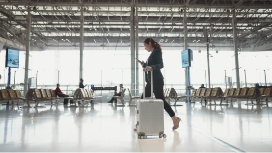A businesswoman walking through an airport with a sleek, polished hairstyle, demonstrating how a hair wax stick creates a travel-ready, professional look in minutes.