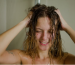 A woman with wet, frizzy hair in the shower, illustrating the humidity-related hair challenges a hair wax stick can solve.